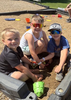 Three kids at the park playing together in the sand box.