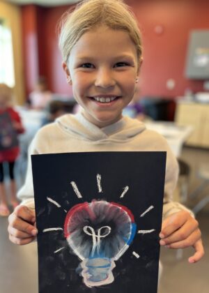photo of a girl holding up her artwork of a lightbulb