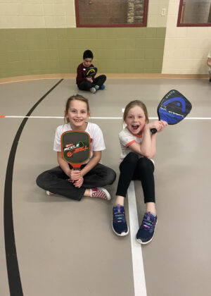 photo of two girls sitting and holding pickleball paddles