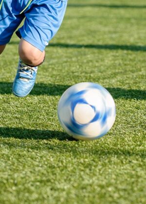 Photo showing a youth running on a soccer field with a soccer ball.
